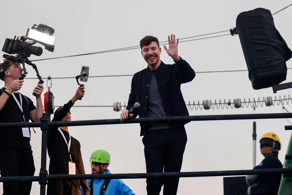 MrBeast waving from a set at dusk while camera operators film beside him