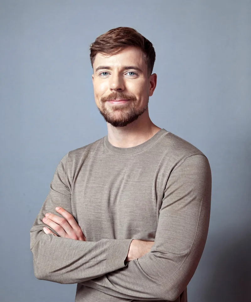 Portrait of MrBeast in a grey sweater, arms crossed, smiling